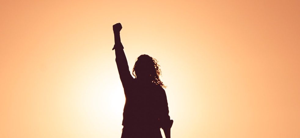 Silhouette of a motivational figure with fist in the air against a sunset